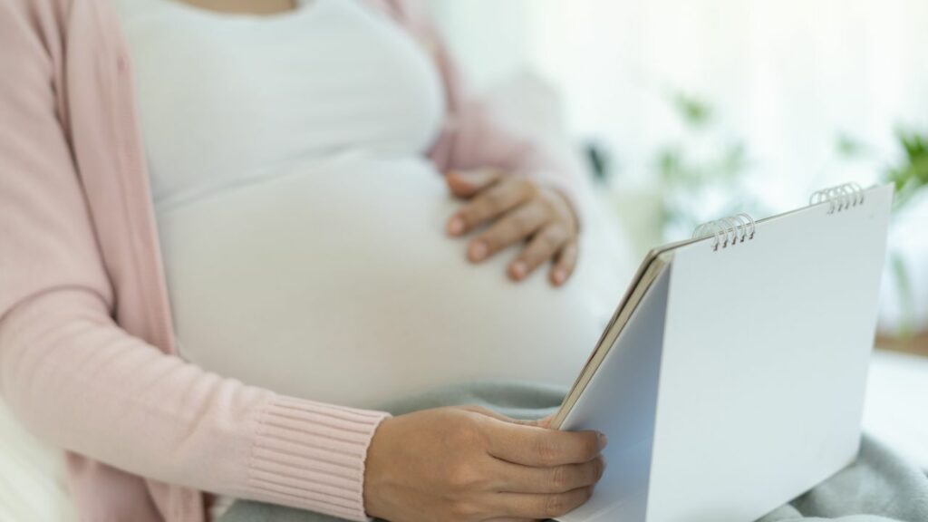 woman looking at a calendar while holding her pregnant belly.