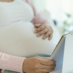 woman looking at a calendar while holding her pregnant belly.